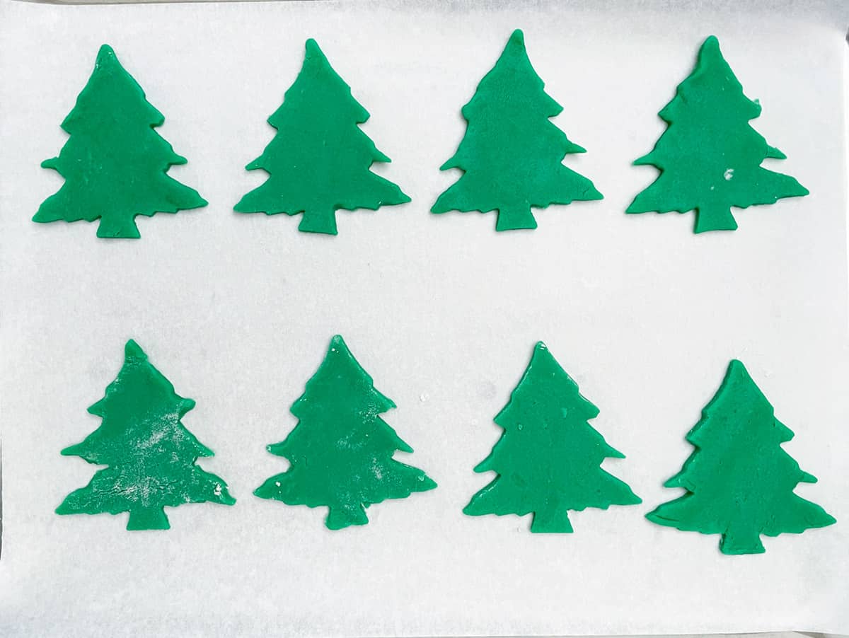 Christmas tree sugar cookie dough cut out into Christmas tree shapes and on a cookie sheet pan.
