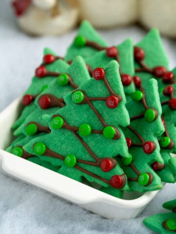 Christmas tree sugar cookies in white serving bowl on fake snow.