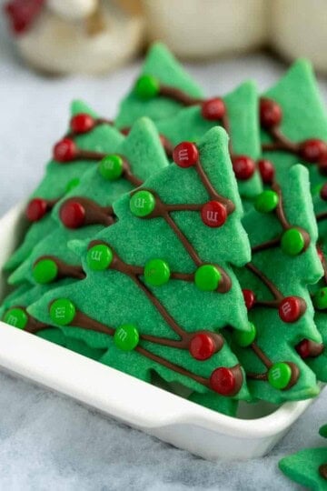 Christmas tree sugar cookies in white serving bowl on fake snow.