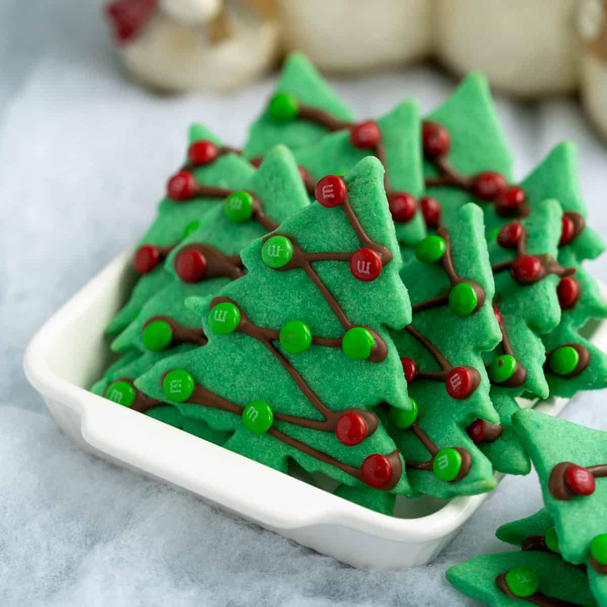 Christmas tree sugar cookies in white serving bowl on fake snow.