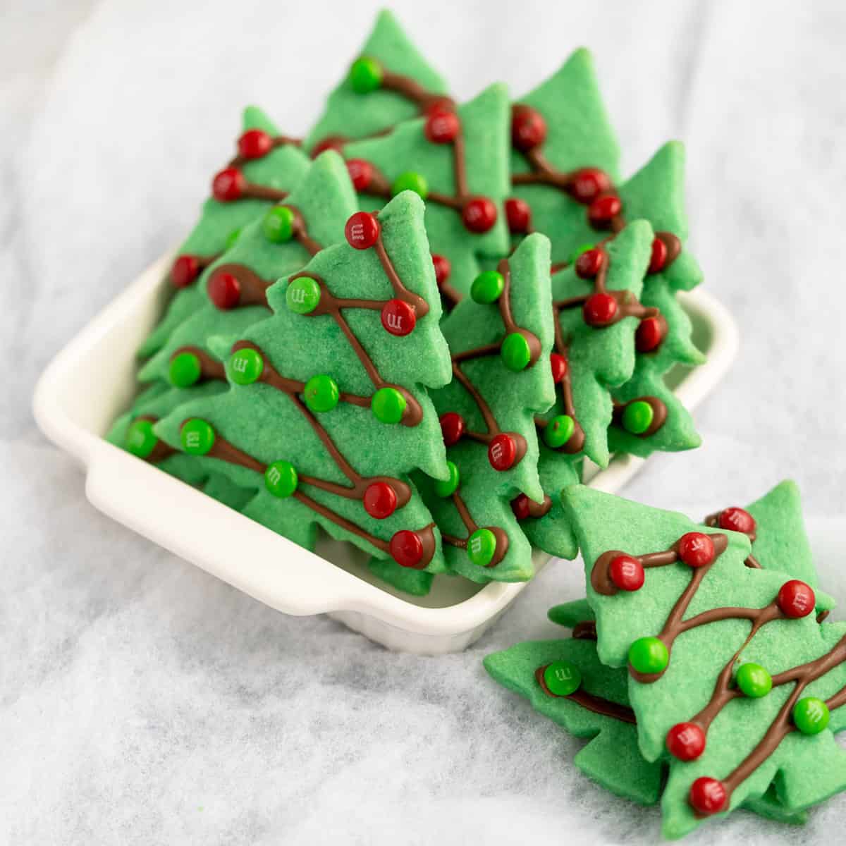 Christmas tree sugar cookies close-up with M&M decorations in white serving bowl.