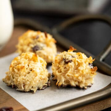 Side view of three baked coconut macaroons on a piece of parchment paper which is on a wooden tray.