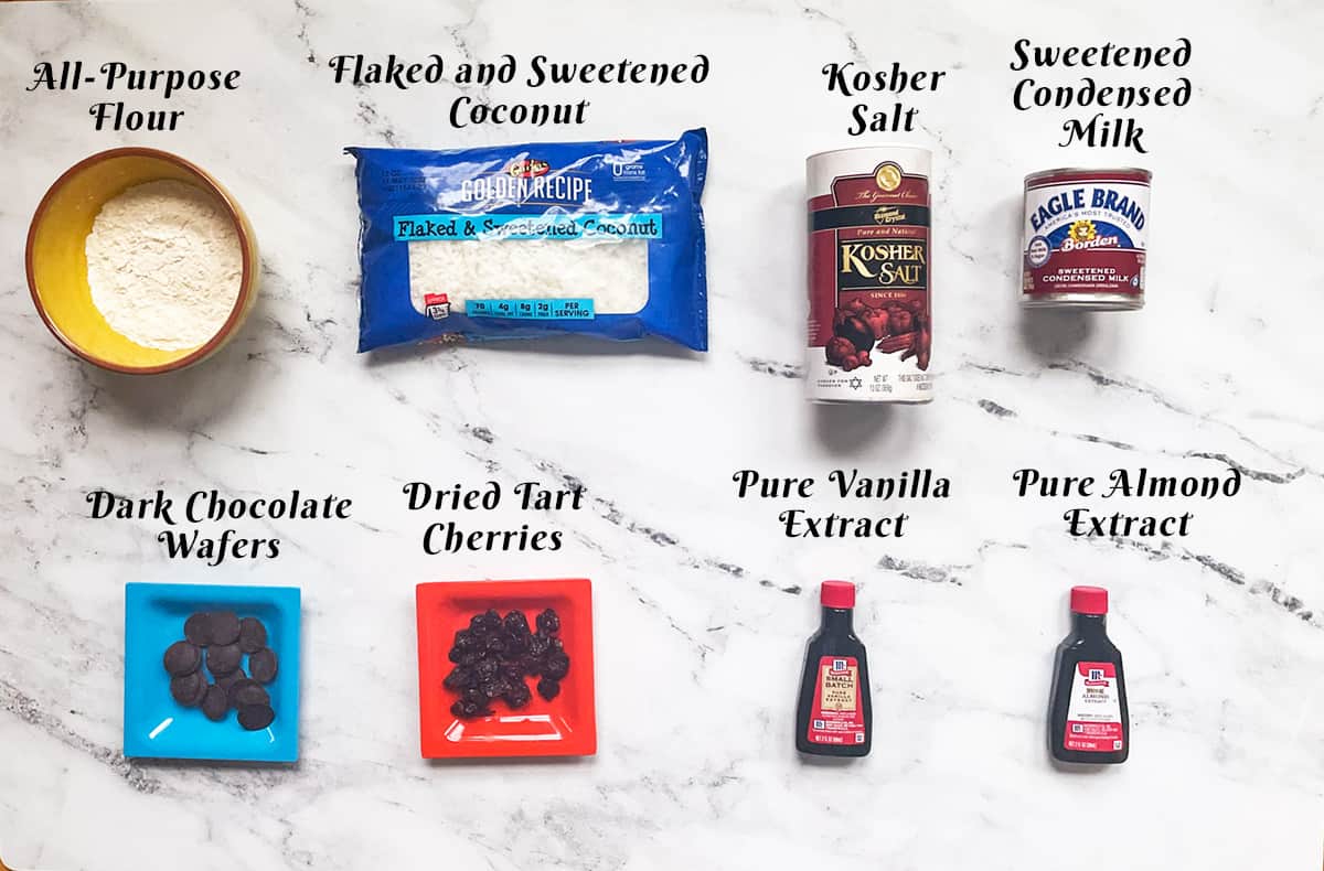Ingredients for Coconut macaroons with cherries and dark chocolate on a marble background.