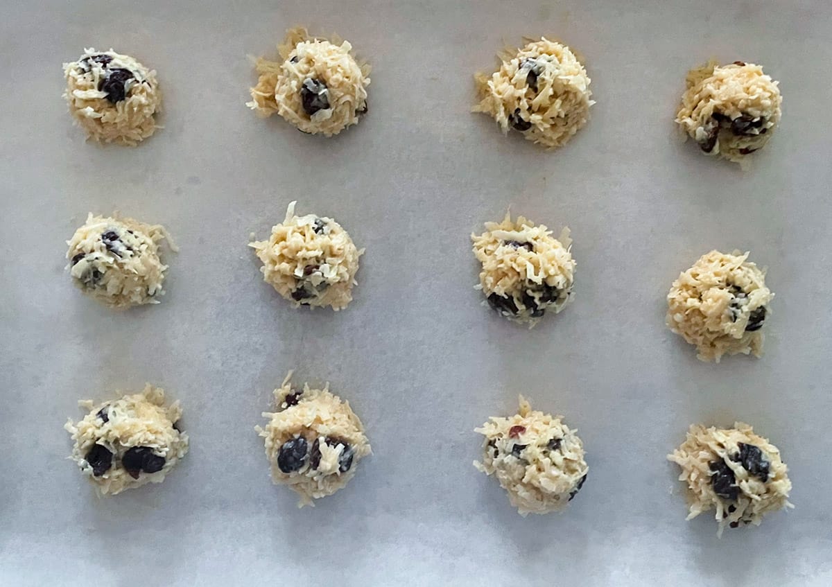 Twelve mounds of coconut macaroons on parchment paper ready for the oven.