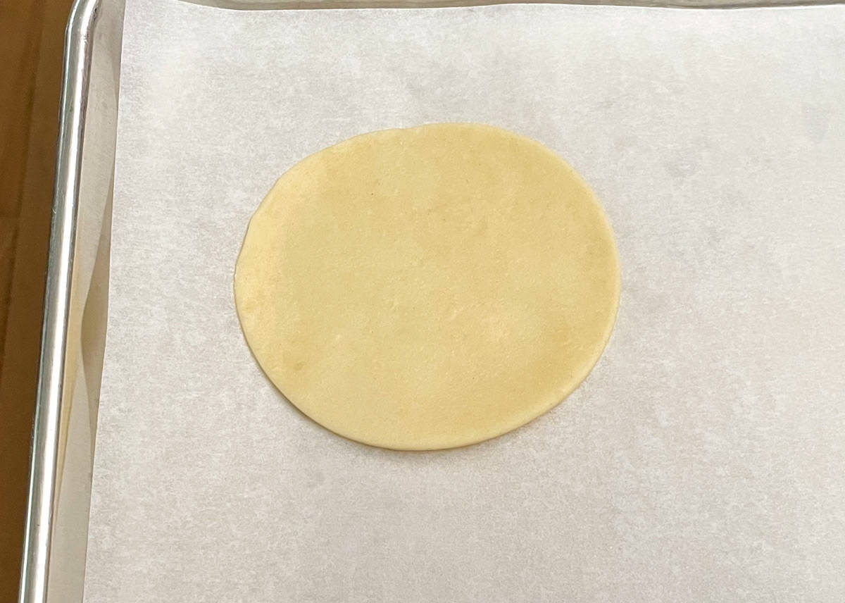 A 4-inch round cutout of cookie dough on parchment paper.