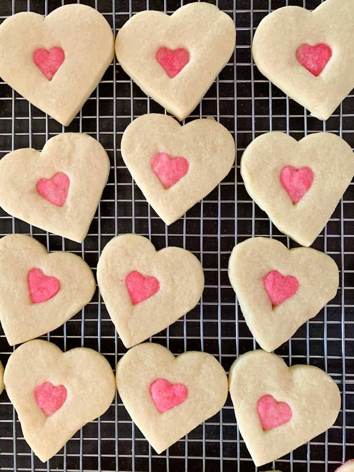 Baked 2 heart cookies on a cooling rack, small pink heart in the middle of a larger white heart.