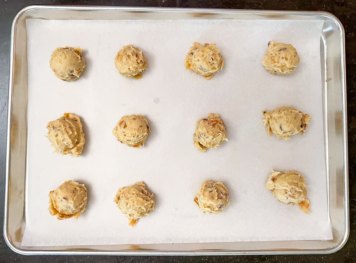 Twelve cookie scoops on a parchment-linded cookie sheet pan.
