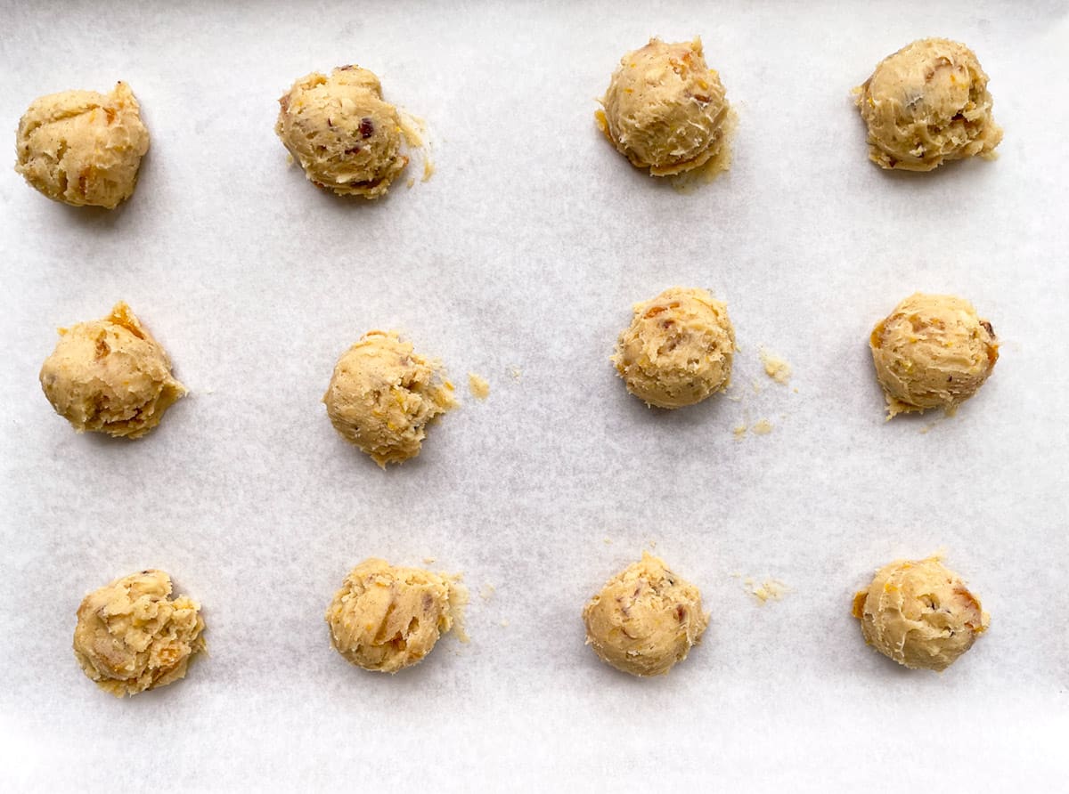 Twelve scoops of raw cookie dough on parchment paper.