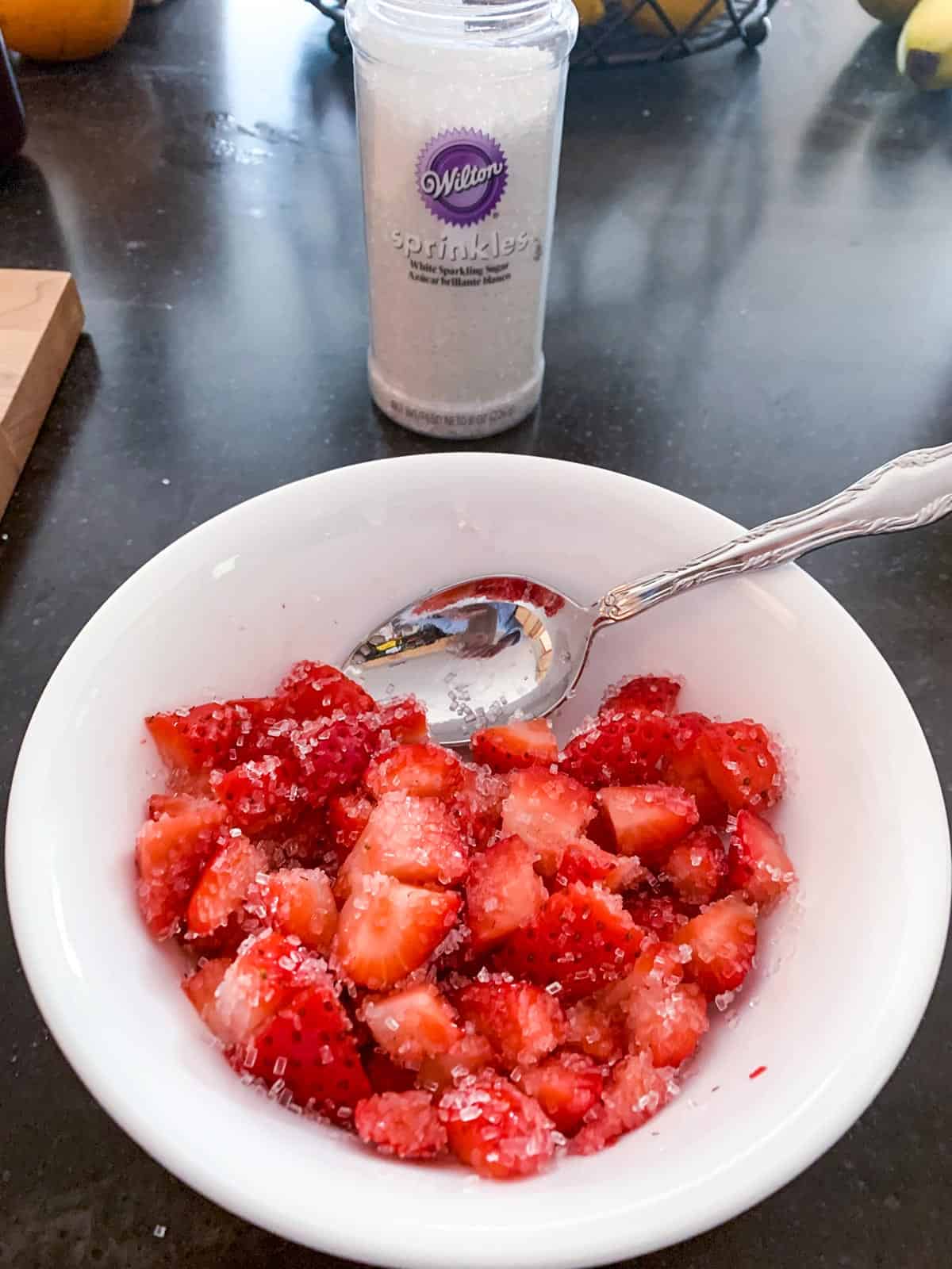 Mixing fresh cut up strawberries with course sprinkle sugar,
