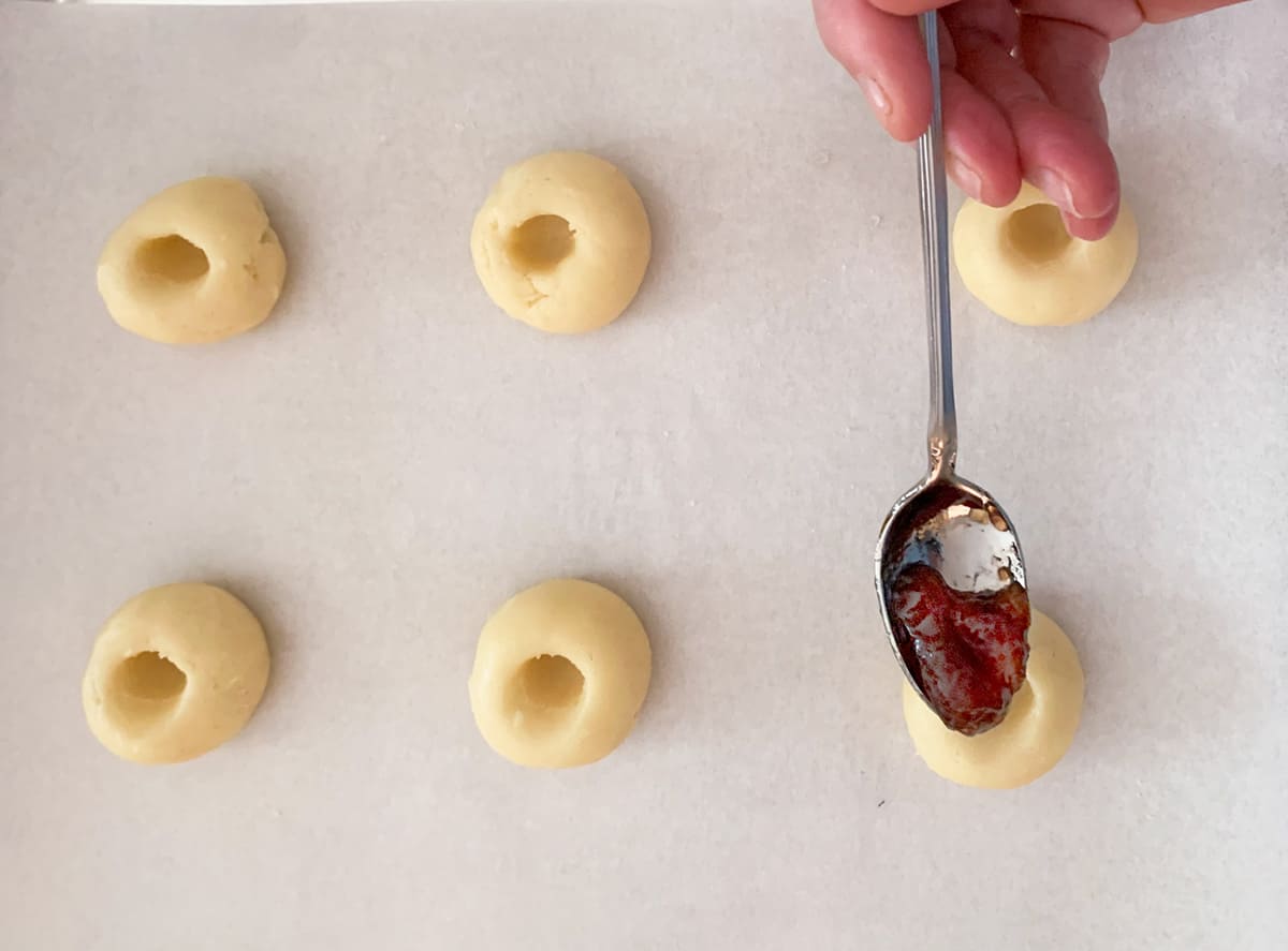 Filling the thumbprint well with a spoonful of jam.