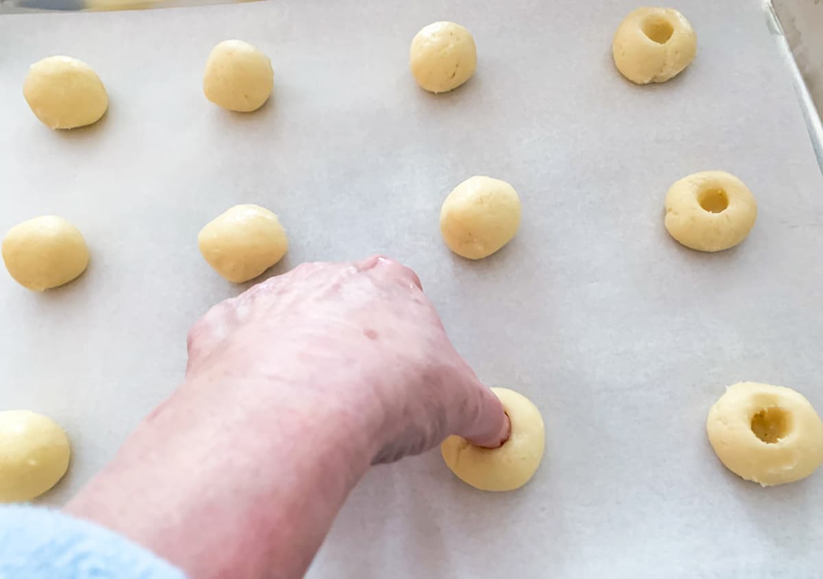 Making a ball of cookie dough and creating a well by taking your thumb straight down through the top.