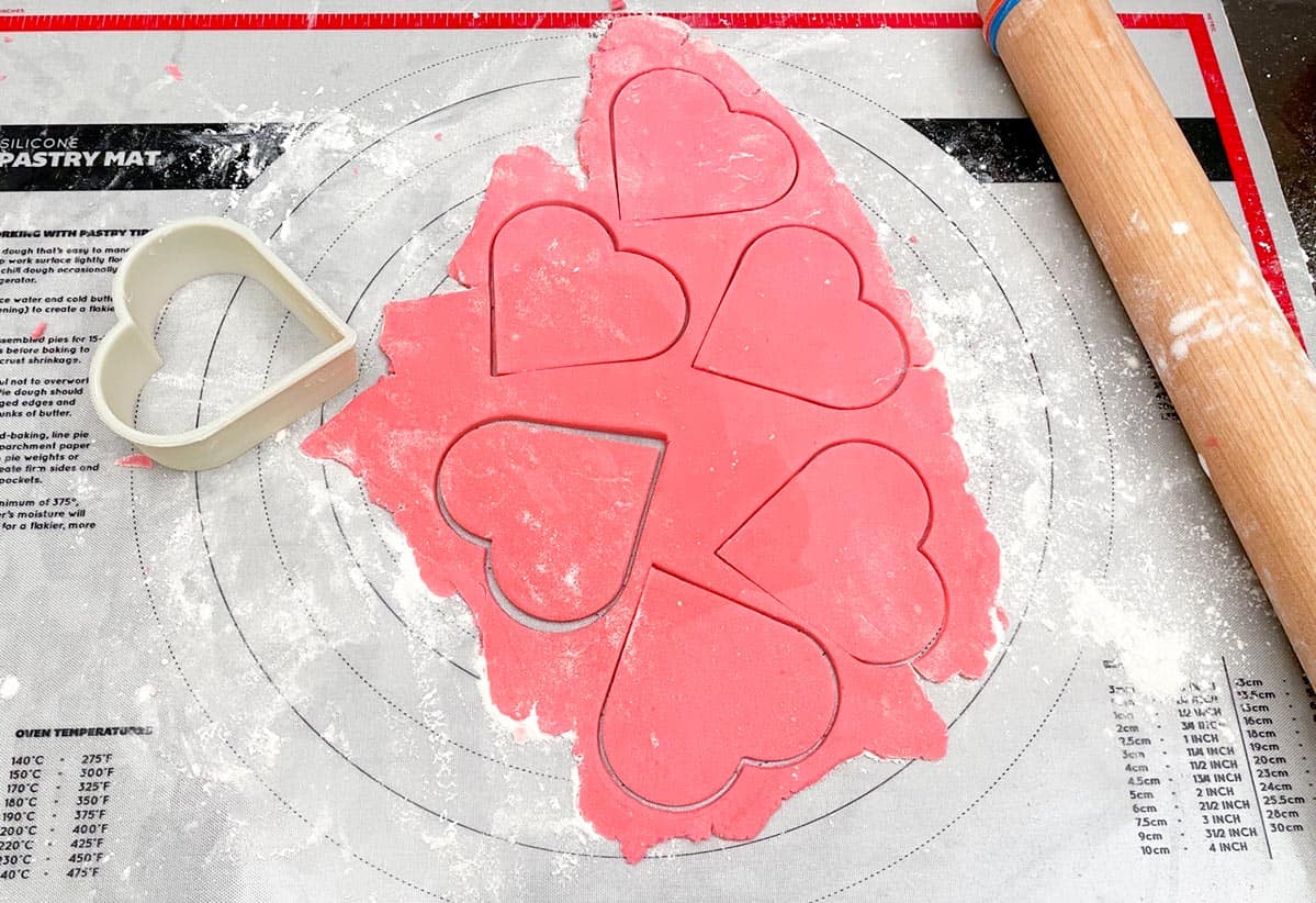 Rolled out pink sugar cookie dough and six heart shapes are cut out with cookie cutter.