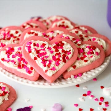 Heart Sugar Cookies with Buttercream Icing on a white plate along with heart candies all around.