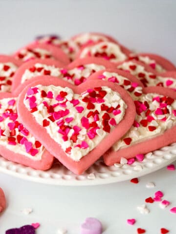 Heart Sugar Cookies with Buttercream Icing on a white plate along with heart candies all around.