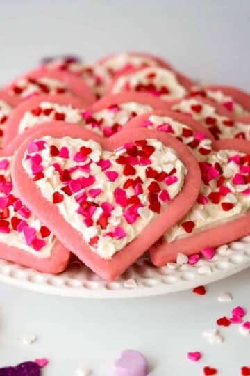 Heart Sugar Cookies with Buttercream Icing on a white plate along with heart candies all around.