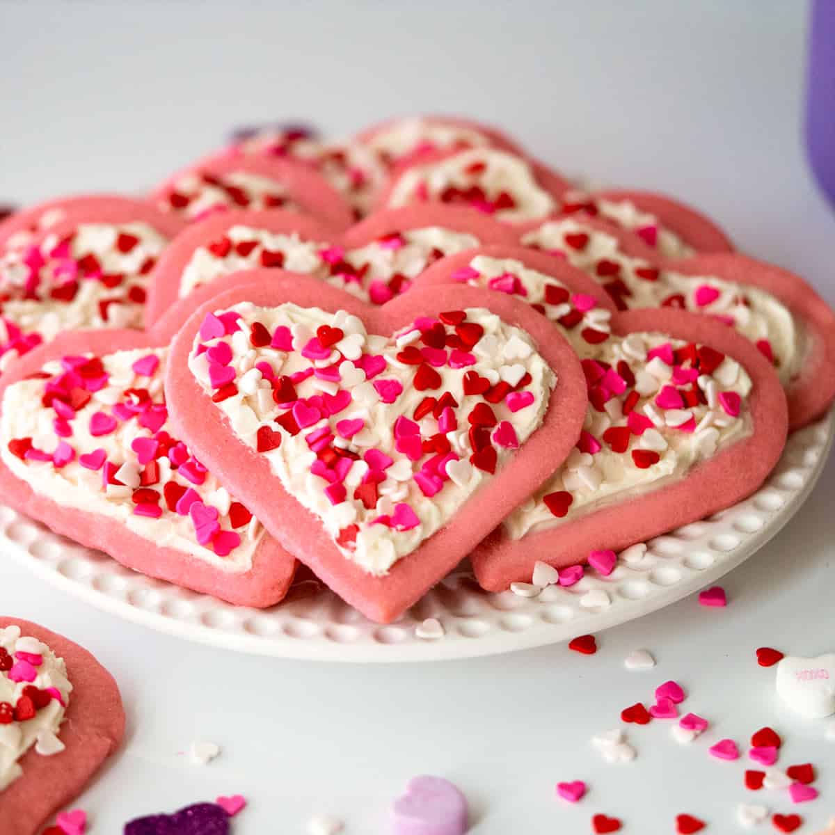 Heart Sugar Cookies with Buttercream Icing on a white plate along with heart candies all around.