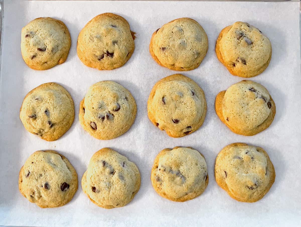 Chocolate Chip Cookies resting on a parchment-lined sheet pan after baking.