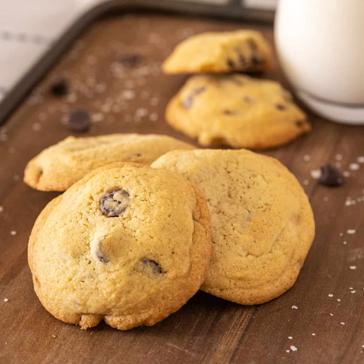 Chocolate chip cookies on a serving board with a glass of milk.