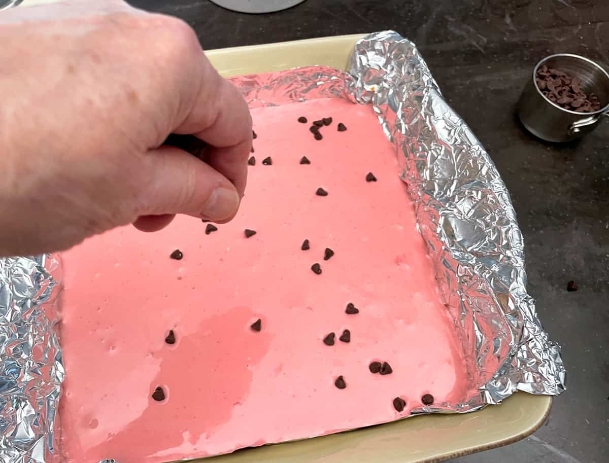 Adding the mini chocolate chips to the top of the strawberry cheesecake before baking.
