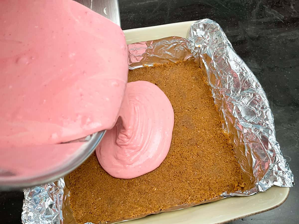 Pouring the strawberry cheesecake mixture onto the pressed down graham cracker mixture.