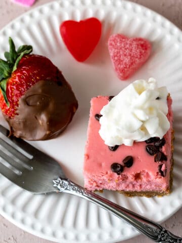 Strawberry and chocolate chip cheesecake bites on a plate with a chocolate covered strawberry.