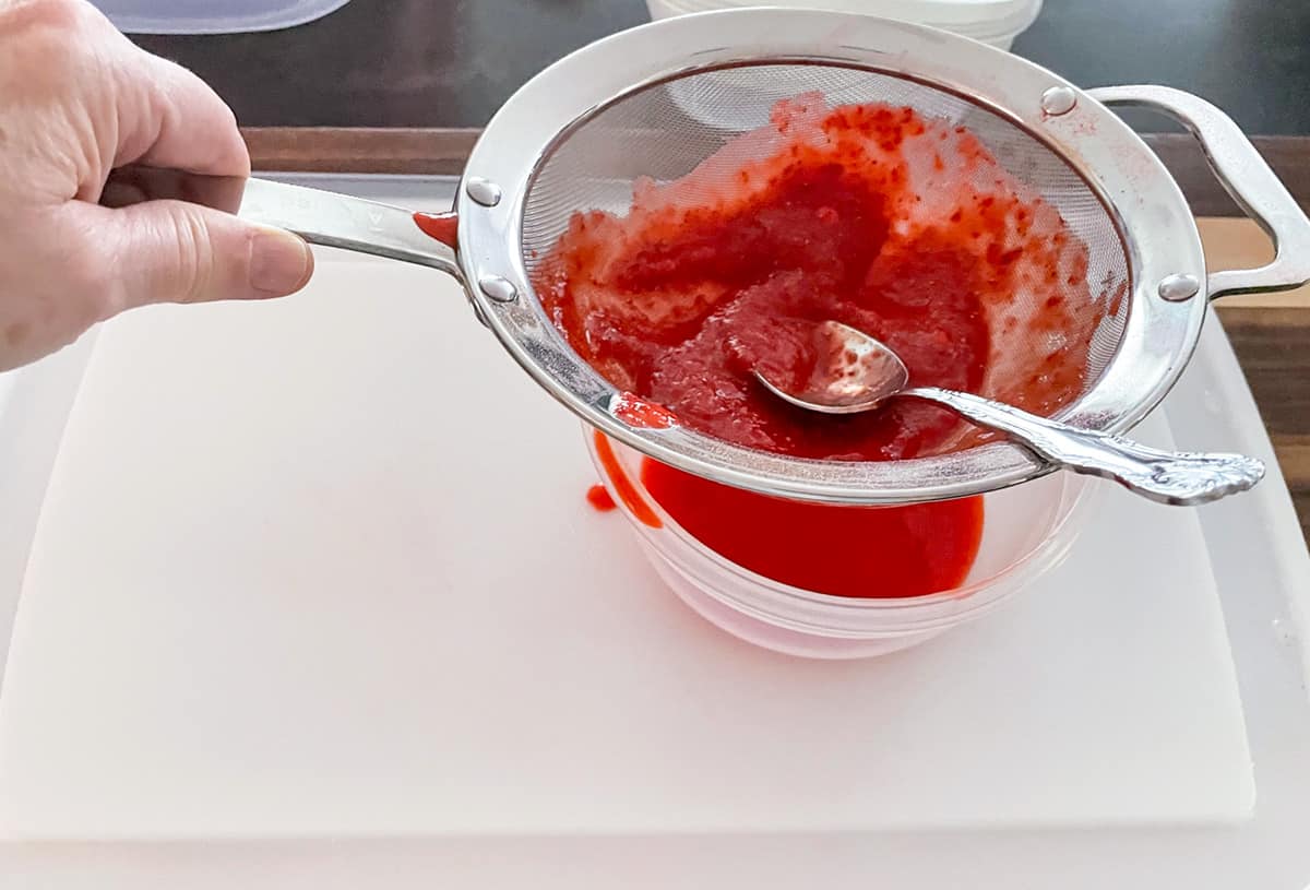 Straining the pureed fresh strawberries to get just the juice and no seeds.