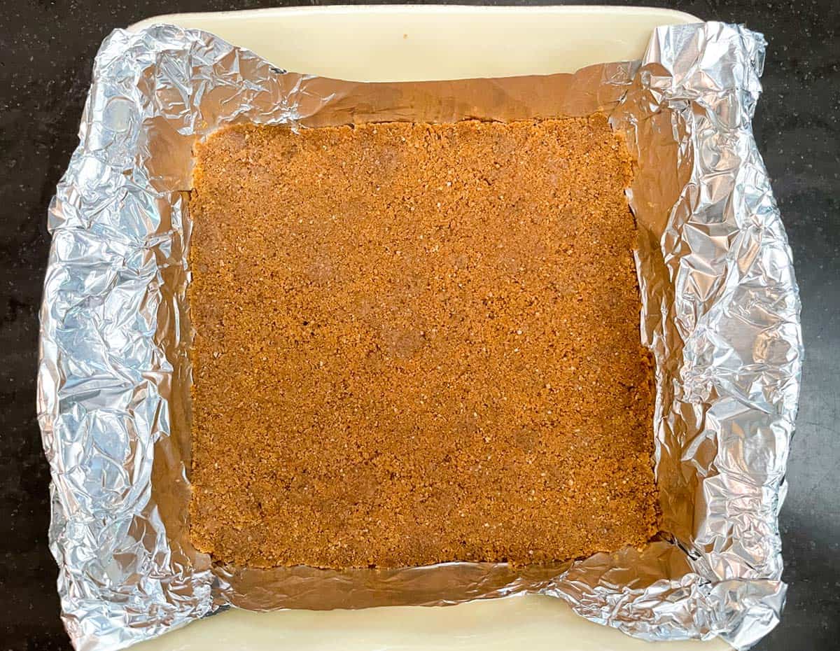 Graham cracker mixture pressed into the bottom of a tin-foiled lined baking dish.