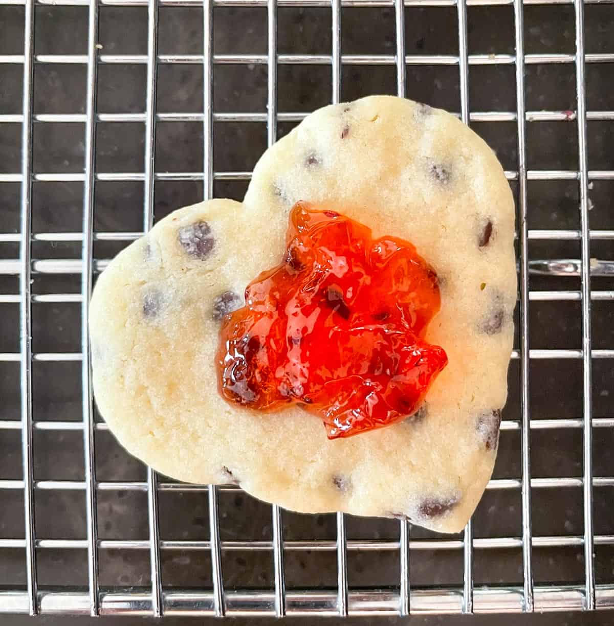 Laying a teaspoon of strawberry jelly on the bottom heart cookie.