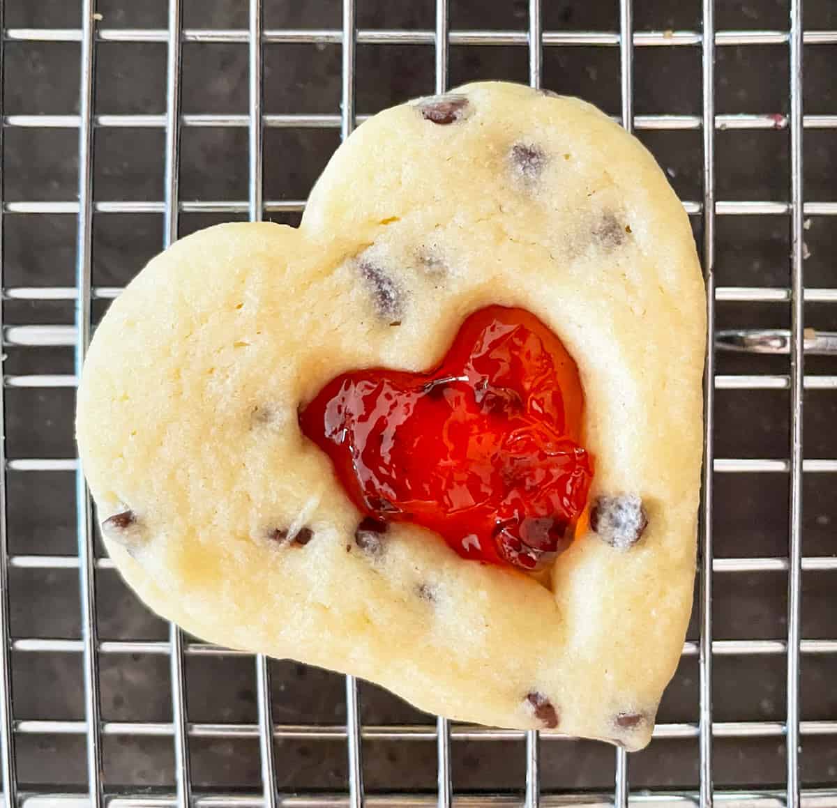 Cookies baked and put together with the strawberry jelly showing through the small heart cutout.