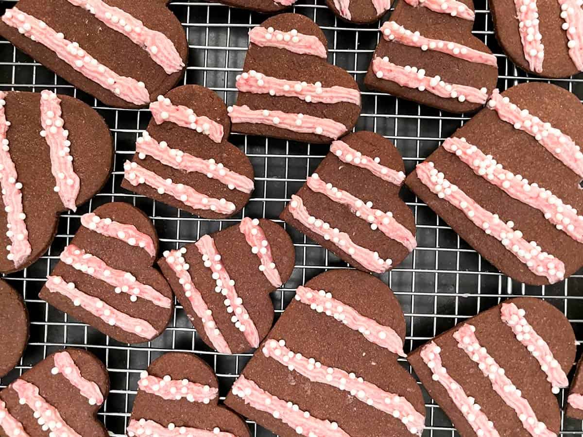 Chocolate cookies with strawberry icing piped in diagonal lines with white penile sprinkles on the icing.