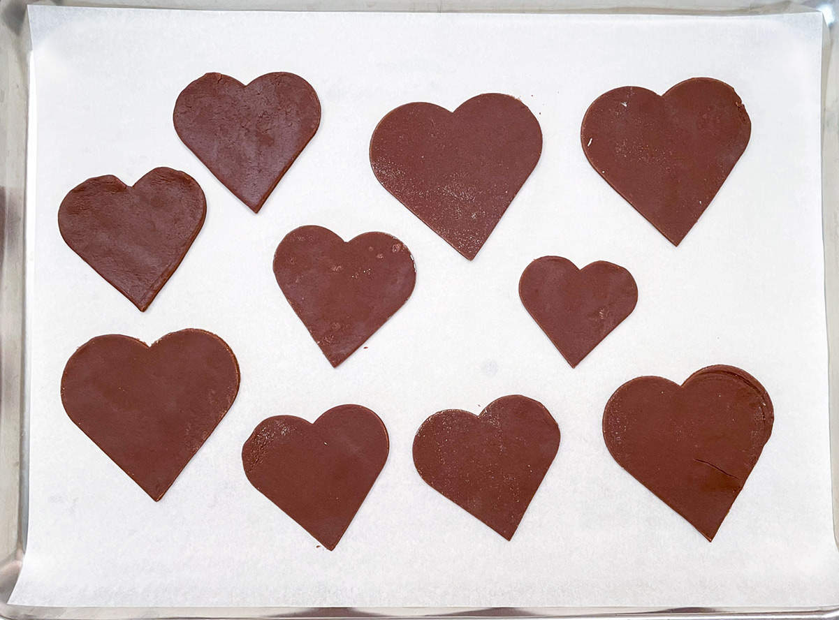Ten chocolate heart cookies on parchment-lined cookie sheet pan.