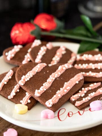 Heart chocolate cookies with strawberry icing on a white plate with the word LOVE on it.