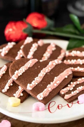 Heart chocolate cookies with strawberry icing on a white plate with the word LOVE on it.