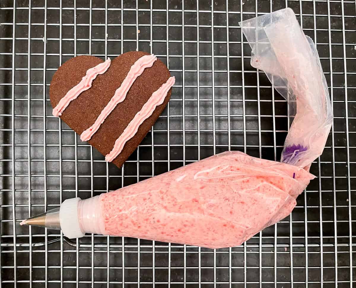 Piping bag with tip and a cookie with 3 stripes of the icing on top.