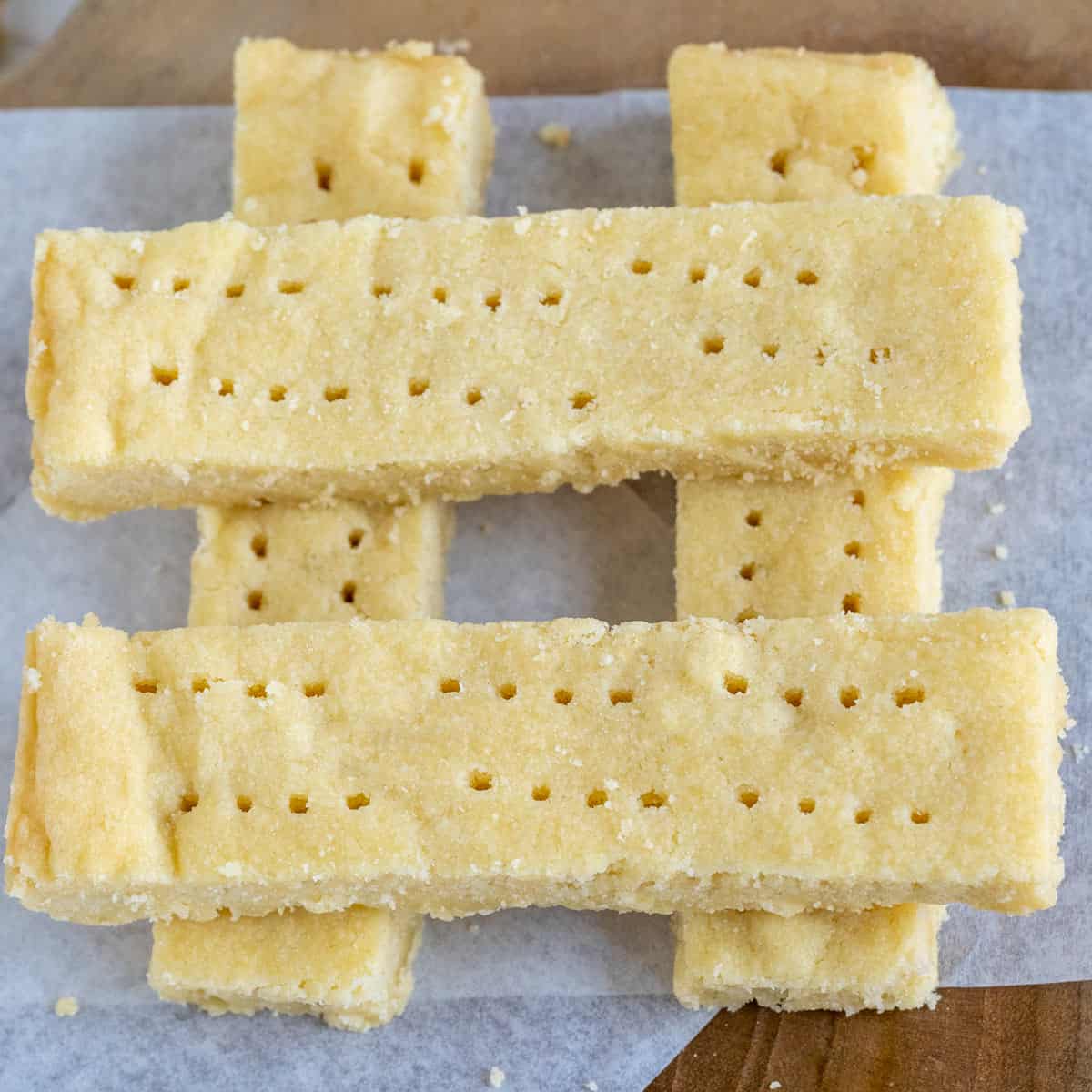 Four Scottish shortbread cookies in a crisscross pattern square piece of parchment paper.