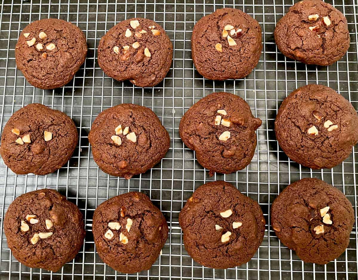 Twelve chocolate cookies on a wire rack cooling after coming out of the oven.