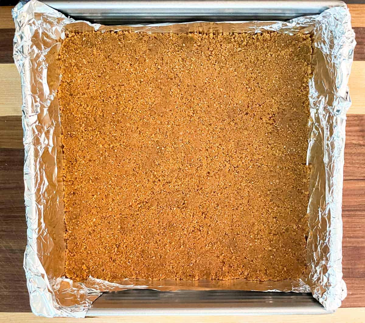 Pressed graham cracker crust onto a foil lined square baking pan.