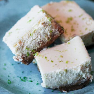 Key lime Cheesecake bars with flacks of lime zest on a blue plate.
