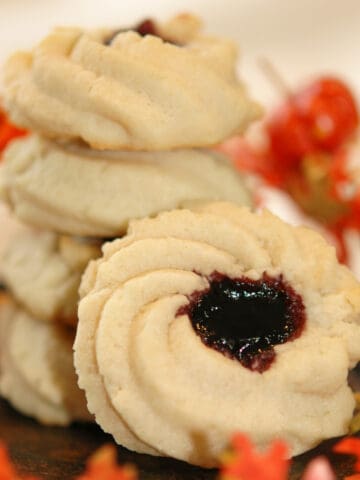 Shortbread cookie with jam with fall leaves around a stack of baked shortbread cookies with jam.