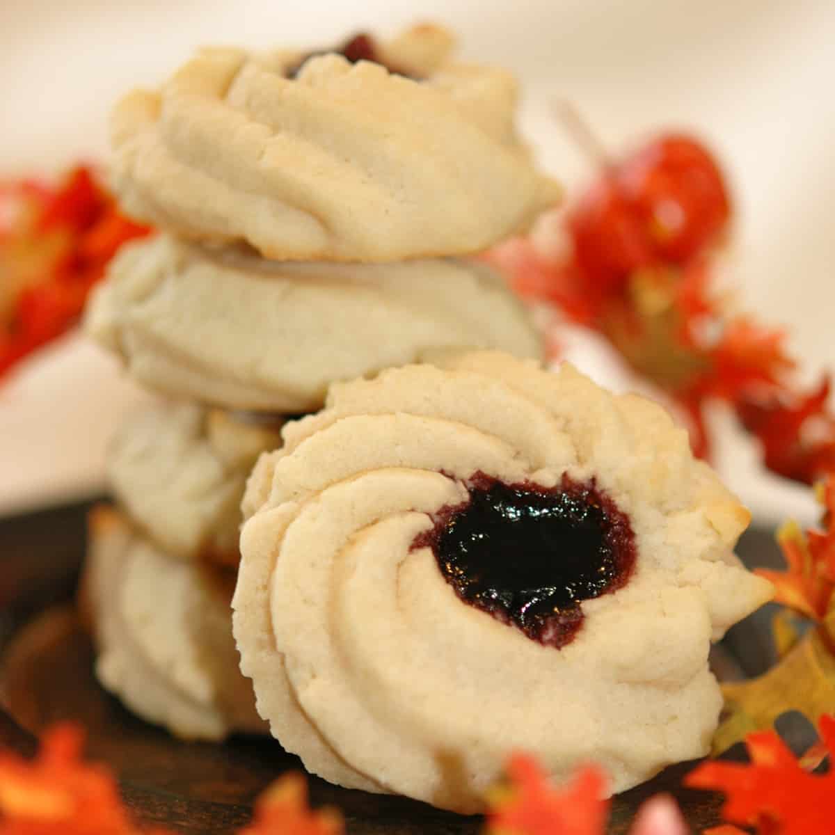 Shortbread cookie with jam with fall leaves around a stack of baked shortbread cookies with jam.