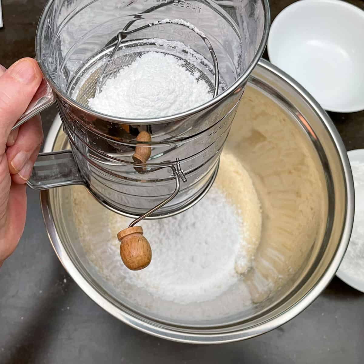 Sifting powdered sugar into a bowl that has almond flour in it.