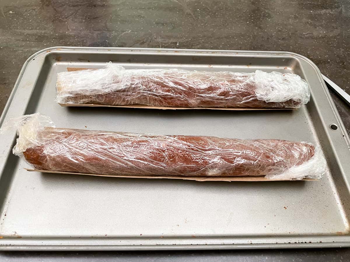 Two cookie logs wrapped in plastic and cradled in paper towel halves.