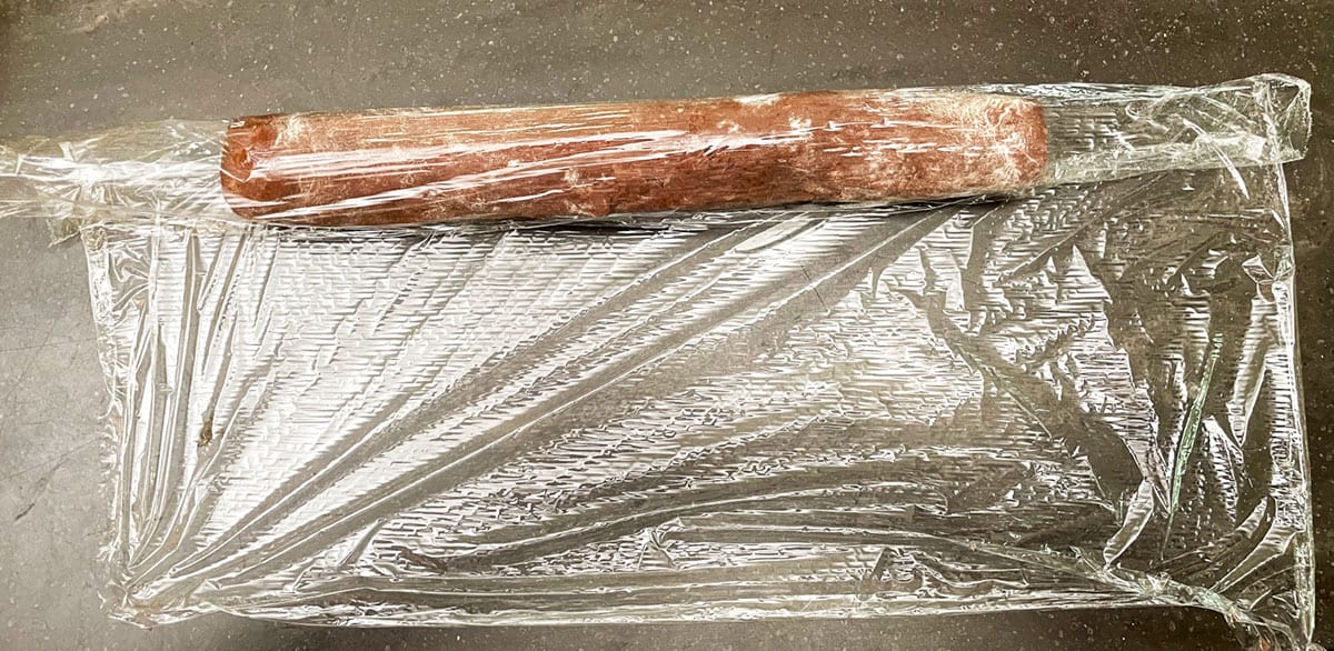 Chocolate shortbread log getting wrapped with plastic wrap.