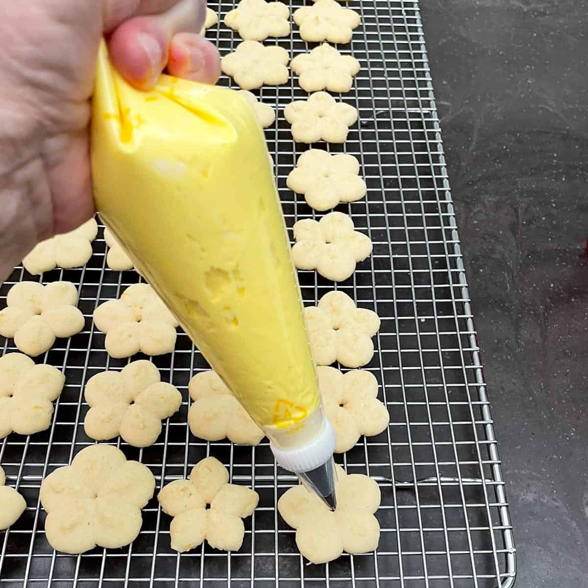 Adding lemon icing onto finished small flower cookies.