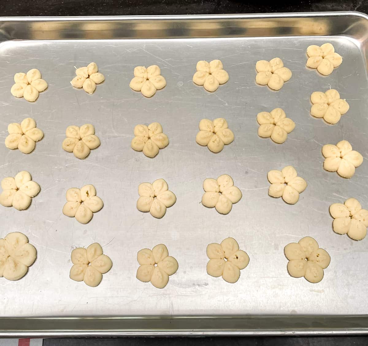 Spritz flower cookies on a cookie sheet pan ready for the oven.