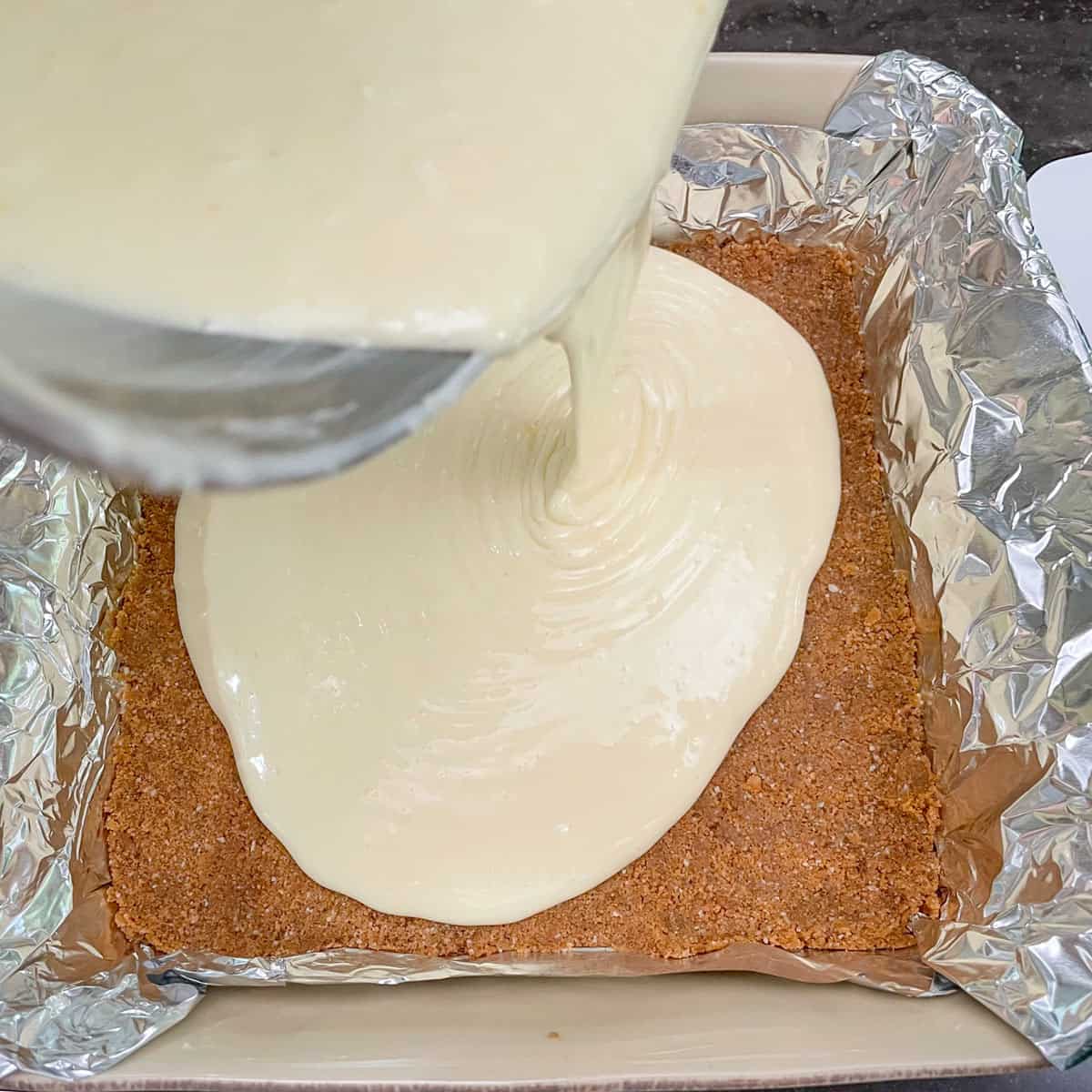 Pouring the cheesecake batter onto the graham cracker crust.