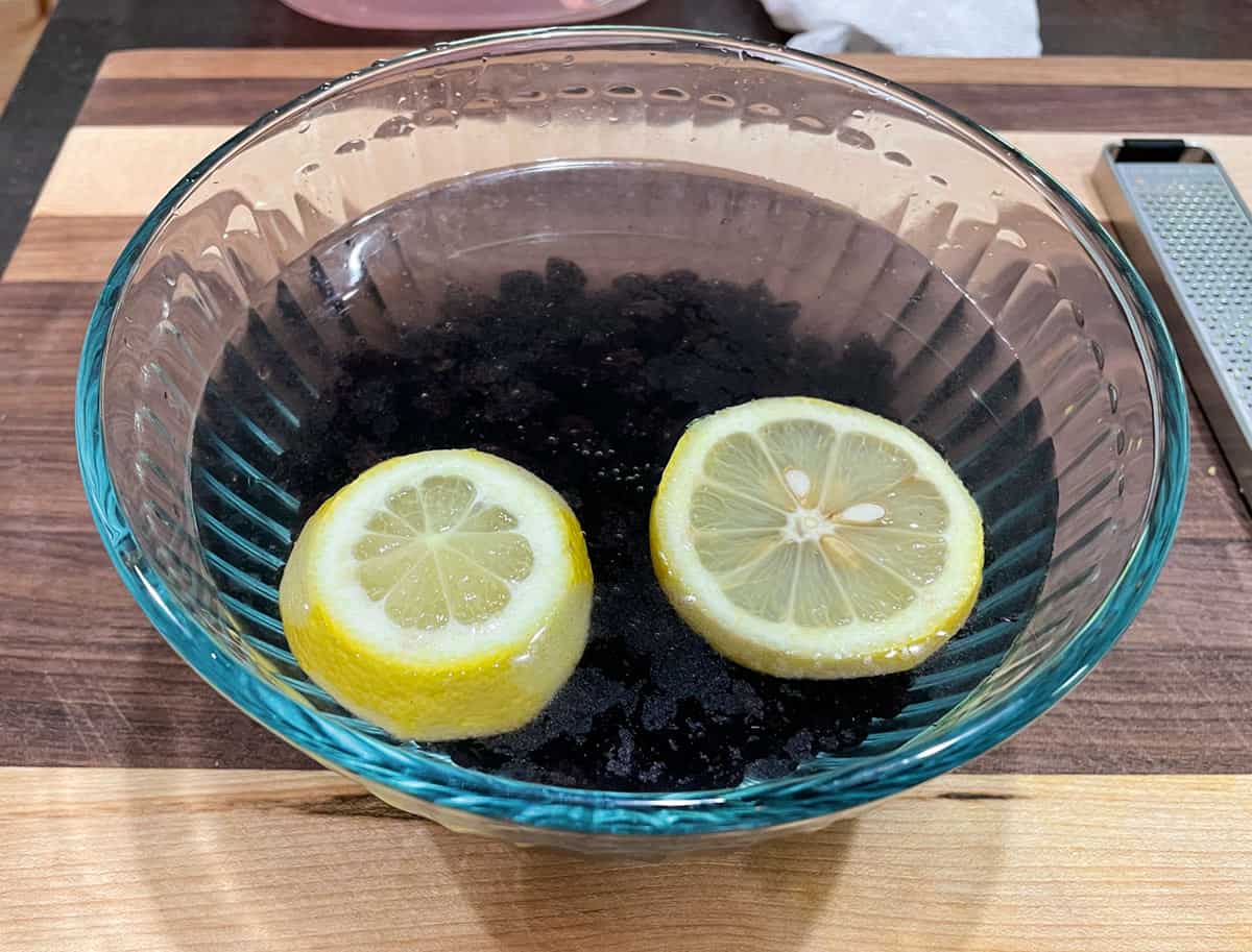 A bowl with dried blueberries soaking in water and 2 lemon slices.