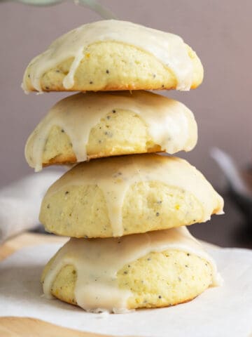 Glazed ricotta orange cookies stacked sitting a piece of parchment paper.