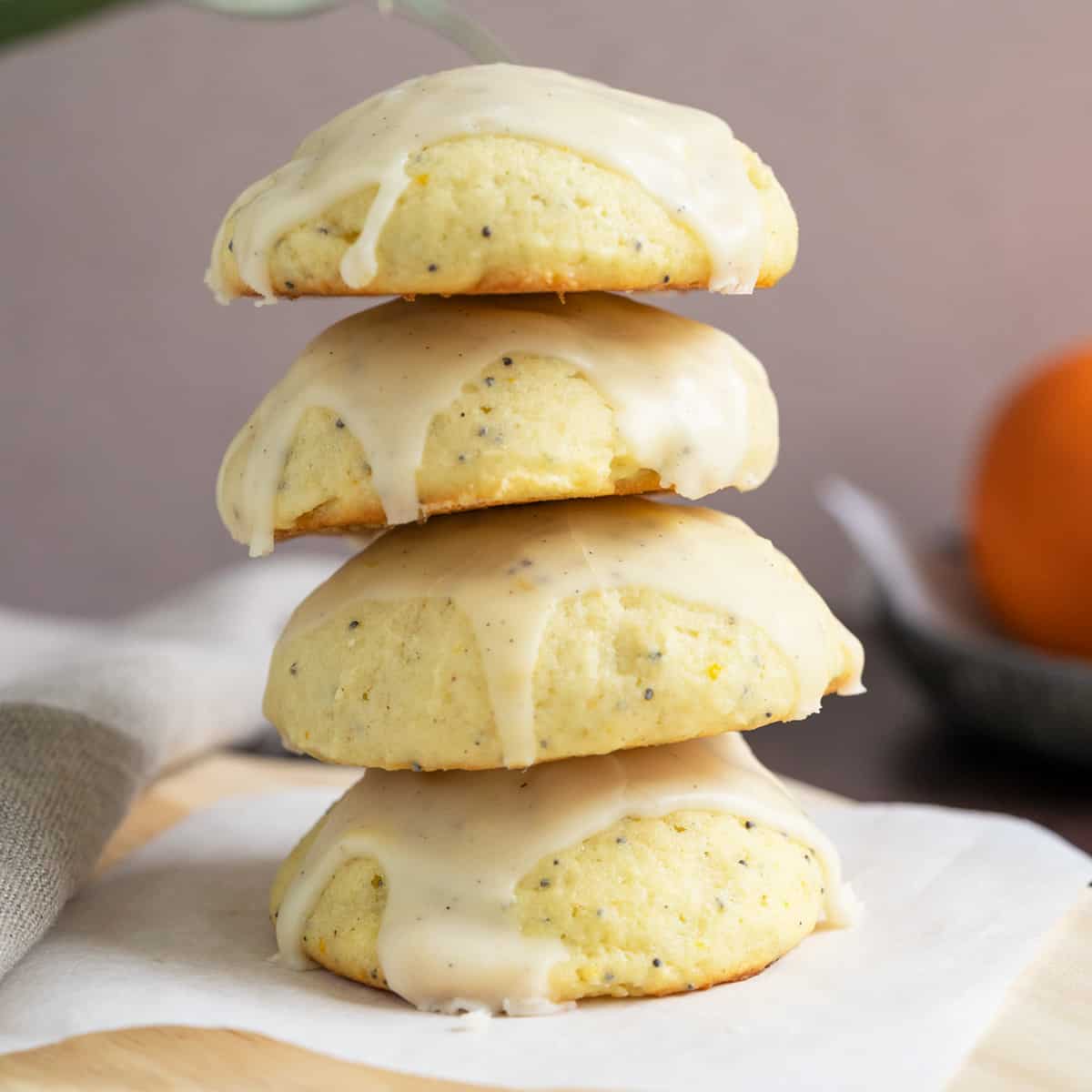 Glazed ricotta orange cookies stacked sitting a piece of parchment paper.