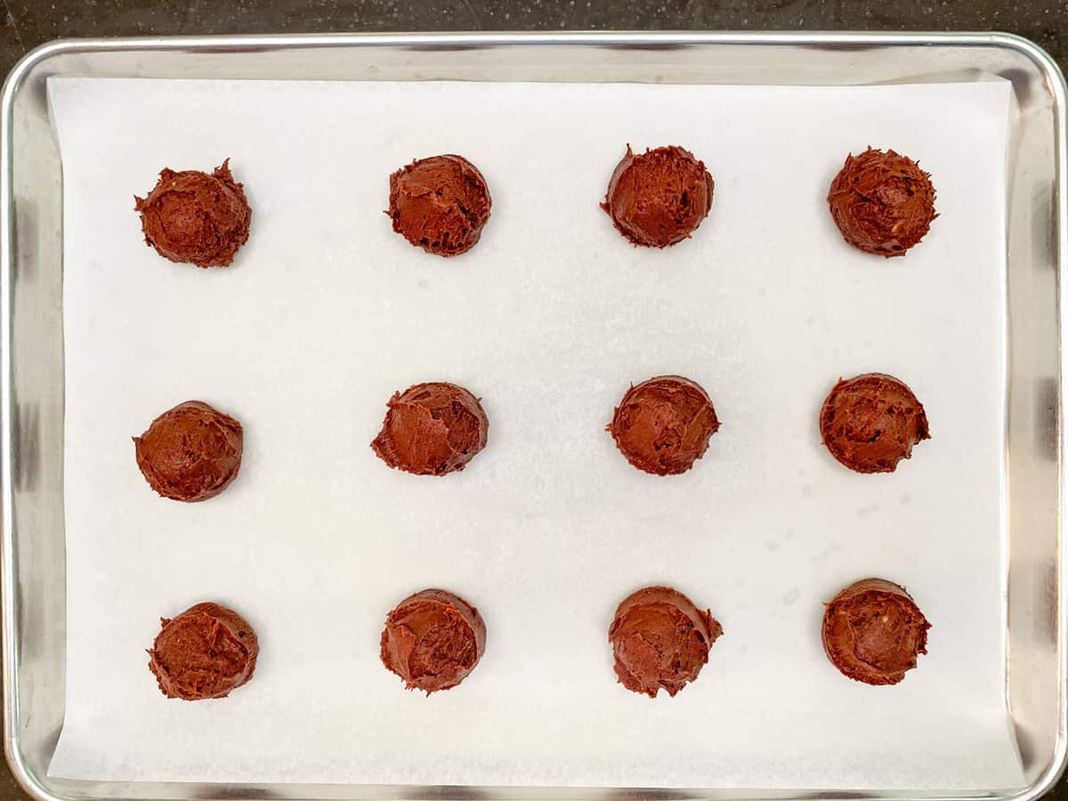 Twelve scooped cookie dough mounds on parchment-lined sheet pan.